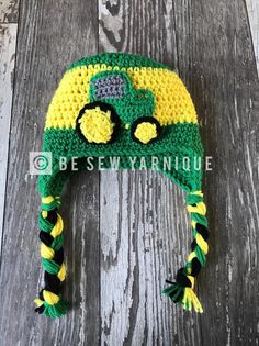 a green and yellow crocheted hat with a tractor on the front, sitting on top of a wooden floor