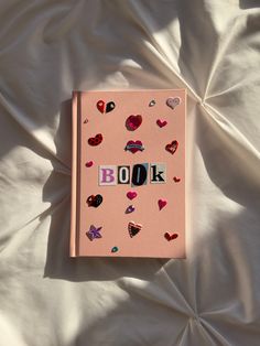 a pink book with hearts on it sitting on top of a white bed sheet covered in sheets