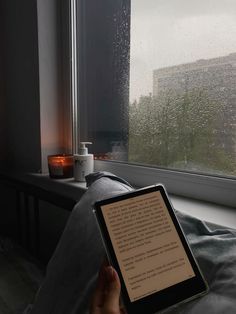 a person holding an electronic device in their hand near a window with rain drops on it