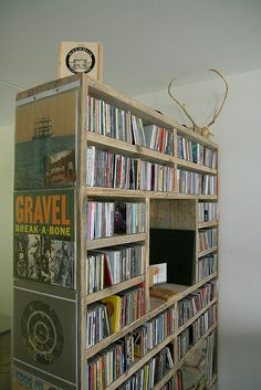 a wooden book shelf filled with dvd's and cds next to a wall mounted television