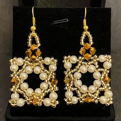 a pair of gold and white beaded earrings sitting on top of a black stand