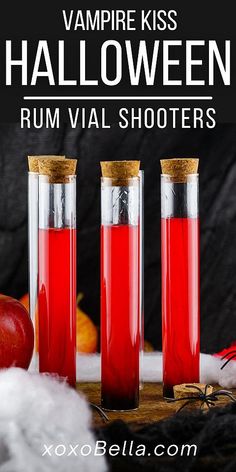 three bottles filled with red liquid next to an apple and cinnamon on a wooden table