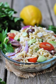 a bowl filled with pasta salad on top of a wooden table next to lemons