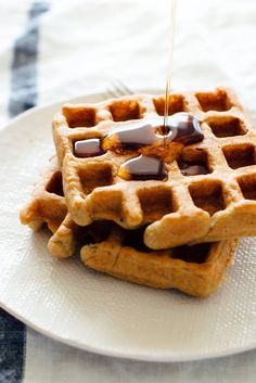 waffles with syrup being drizzled over them on a white plate