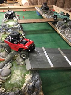 two toy trucks driving over a bridge on top of rocks and grass in a play area