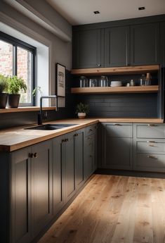 a kitchen with wooden flooring and gray cabinetry next to a large window that has potted plants on it