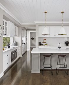 a kitchen with white cabinets and counter tops, two stools in front of the island