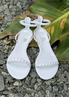 Aria Sandal - Women’s Flat Strappy Sandals in White. Lightweight, cute, and oh-so-comfortable. The flat, strappy Aria White Sandal is a travel essential and a staple of any fashionista’s closet. The best part? It’s completely waterproof, thanks to its jelly form. Take them all over the world—from the beaches of Mexico to the streets of Thailand. Or simply wear them with your favorite comfy outfit for a walk around your neighborhood! With its minimalist straps and compact design, the Aria Sandal Summer T-strap Sandals With Flat Heel And Adjustable Strap, Summer Jelly Sandals With Adjustable Strap, Summer Synthetic Jelly Sandals With Adjustable Strap, White Flat Sandals With Adjustable Strap, Summer Jelly Sandals With Adjustable Strap And Round Toe, Adjustable Ankle Strap Jelly Sandals For Beach, White Flat Heel Jelly Sandals For Vacation, Summer Vacation T-strap Sandals With Adjustable Strap, White Sandals With Adjustable Strap For Vacation