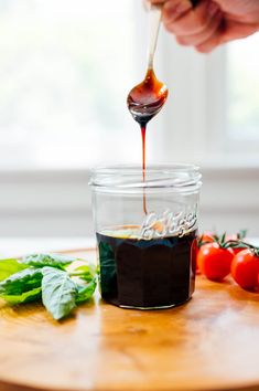 someone is dipping sauce into a glass jar with tomatoes and basil on the table next to it