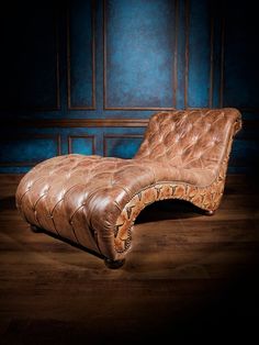 a brown leather chaise lounge chair sitting on top of a hard wood floor next to a blue wall