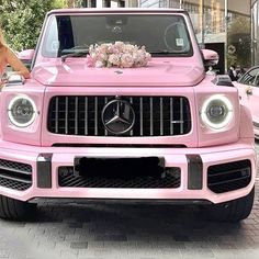 a woman standing next to a pink mercedes benz truck with flowers on the front grill