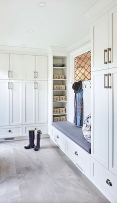 a large white closet with lots of cabinets and boots on the bench next to it