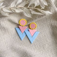 two colorful earrings sitting on top of a white cloth next to some plants and leaves