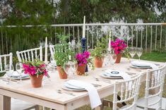 the table is set with white chairs and pink flowers in potted planters on it