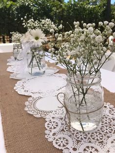 white flowers are in mason jars on a burlock tablecloth with doily