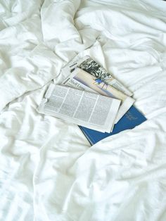 an open magazine laying on top of a white comforter covered bed with sheets and pillows