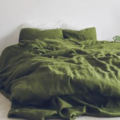 an unmade bed with green linens on top of it and a plant in the corner