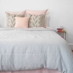 a bed with pink and grey pillows on top of it in a white walled room