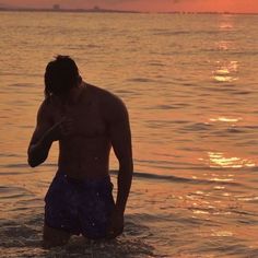 a man standing in the water at sunset with his hand up to his ear and head