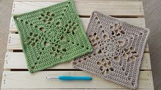 two crocheted squares sitting on top of a wooden pallet next to a knitting needle