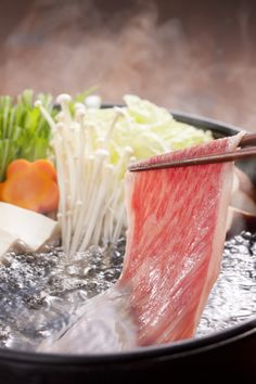 chopsticks are being used to stir up food in a wok with broccoli, lettuce and other vegetables