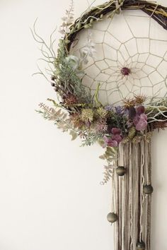 a dream catcher with flowers and plants hanging from it's side on a wall