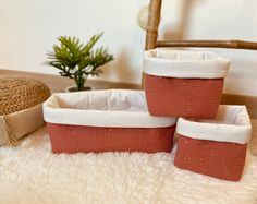 three red and white baskets sitting on top of a fluffy rug next to a potted plant