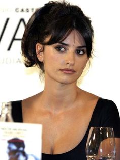 a woman sitting at a table with a glass of wine in front of her and an advertisement behind her