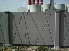 a concrete fence with lines on it and two large tanks in the back ground behind it