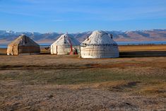 two yurts in the middle of nowhere with mountains in the background and blue sky