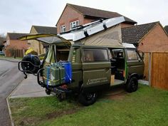 an off road vehicle parked in front of a house with a tent on the roof