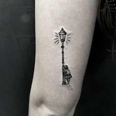 a person standing next to a street light tattoo on the right arm and leg, while holding onto a lamp post