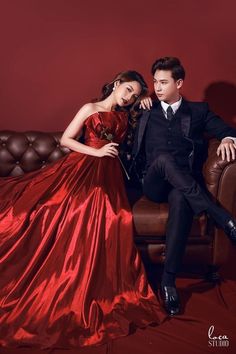 a young man and woman in formal wear sitting on a couch posing for the camera