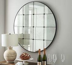 a table topped with bottles of wine next to a lamp and a round mirror on the wall