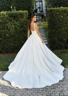 a woman in a white wedding dress is standing on the ground near some hedges and bushes