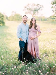 a man and woman standing next to a dog in a field