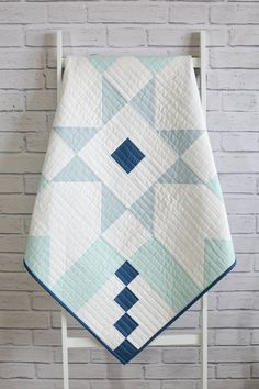 a blue and white quilt sitting on top of a wooden chair next to a brick wall