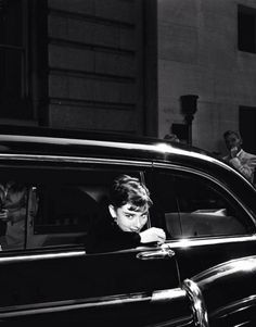 black and white photograph of a man leaning out the window of a car