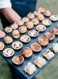 there are many small appetizers on the black tray in front of someone's hand