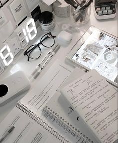 a desk with papers, glasses and alarm clock on it's side next to other office supplies