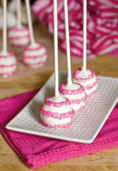 pink and white cake pops are on a plate with some candy sticks in the middle