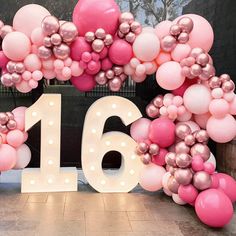 the number sixteen is surrounded by balloons in pink, gold and white colors on display