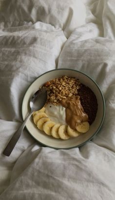 a bowl filled with bananas, granola and peanut butter on top of a bed