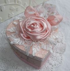 a pink rose sitting on top of a white table cloth next to a heart shaped box