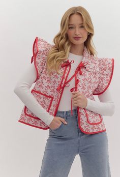 a woman is wearing a red and white vest with flowers on the front, while she has her hands in her pockets