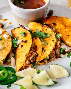 some tacos are sitting on a white plate with limes and peppers next to it