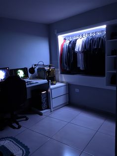 a dimly lit room with clothes hanging on the rack and two computer desks in front of it