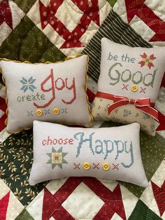 three cross - stitch pillows on a quilted bed with the words be the good and choose happy