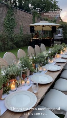 a long table set up with white plates and candles for an outdoor dinner or party