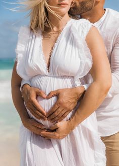 a man and woman standing next to each other on the beach with their hands in their stomach